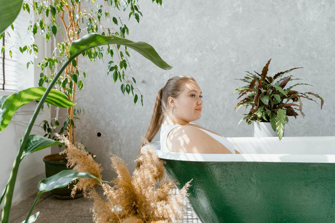 Frau sitzt in einer grünen Badewanne umgeben von Zimmerpflanzen